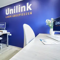 Biuro agencji ubezpieczeniowej Unilink z logo na niebieskiej ścianie, biurkiem i komputerem.