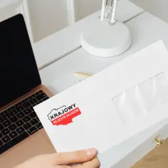 Chcesz wiedzieć, jak sprawdzić czy jestem w KRD? Na biurku leży koperta z logo Krajowego Rejestru Długów, obok laptopa.