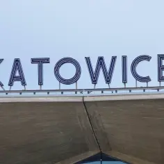 Napis "KATOWICE" z niebieskimi neonami na tle błękitnego nieba.