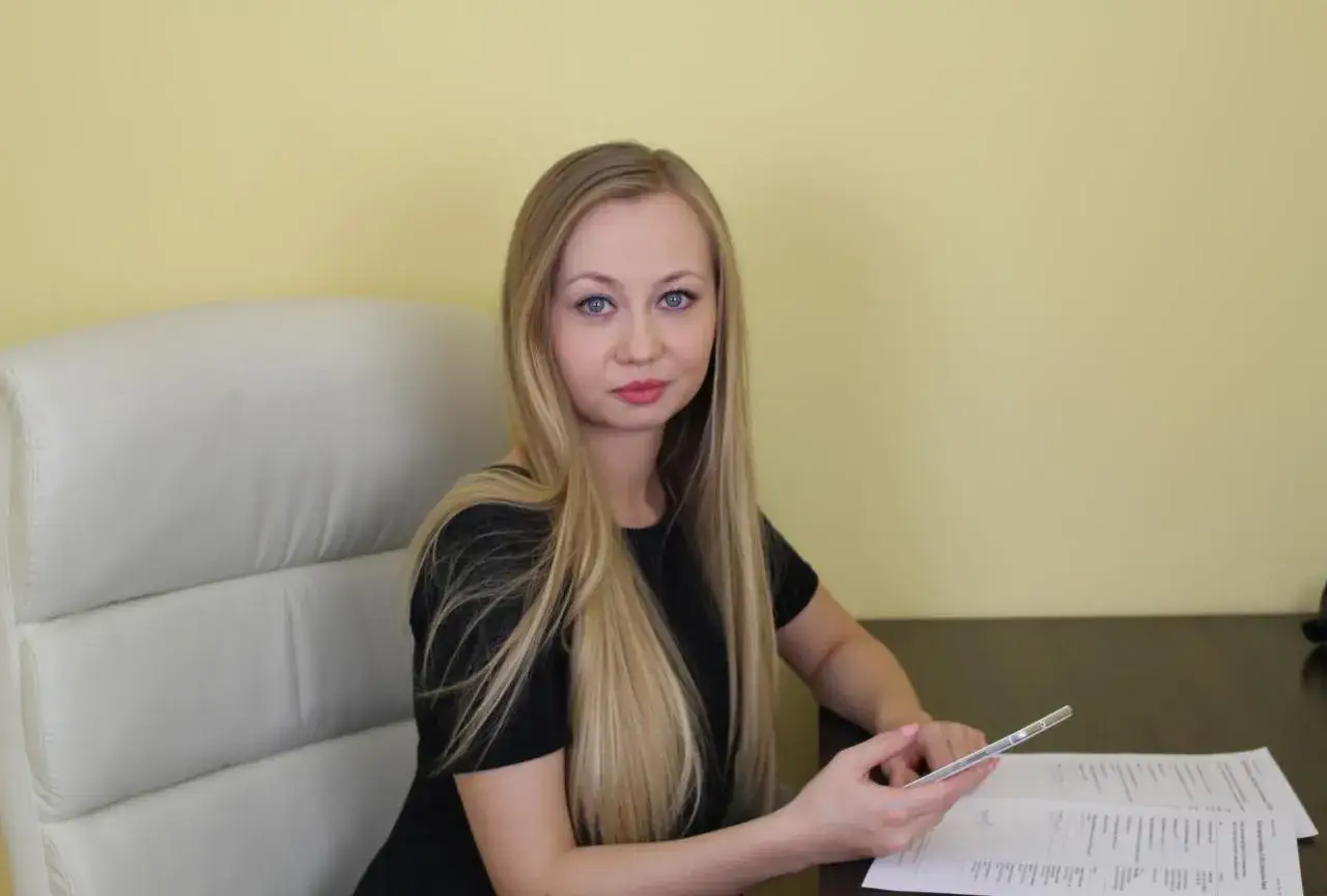 Kobieta z blond włosami siedzi przy biurku, trzymając telefon.