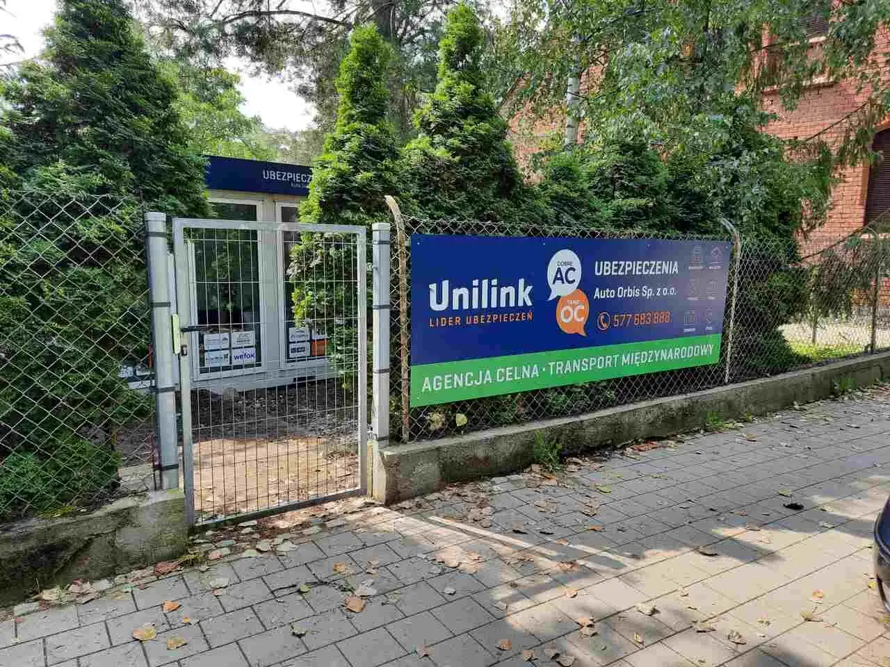 Baner reklamowy ubezpieczeń Unilink i Auto Orbis przed ogrodzeniem.