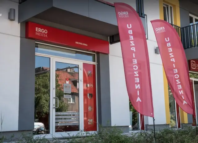 Eleganckie wejście do biura ubezpieczeniowego Ergo Hestia z czerwonym szyldem i dwoma pionowymi banerami.